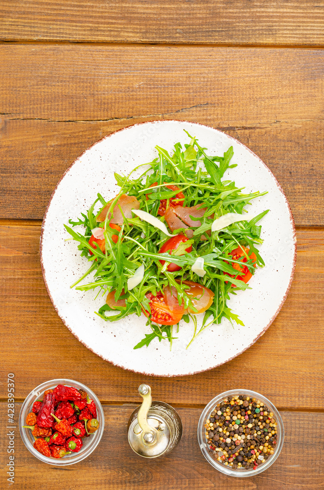 Dish of arugula, tomatoes, dried meat and cheese. Salad on plate on wooden background Dish of arugula, tomatoes, dried meat and cheese. Salad on plate on wooden background