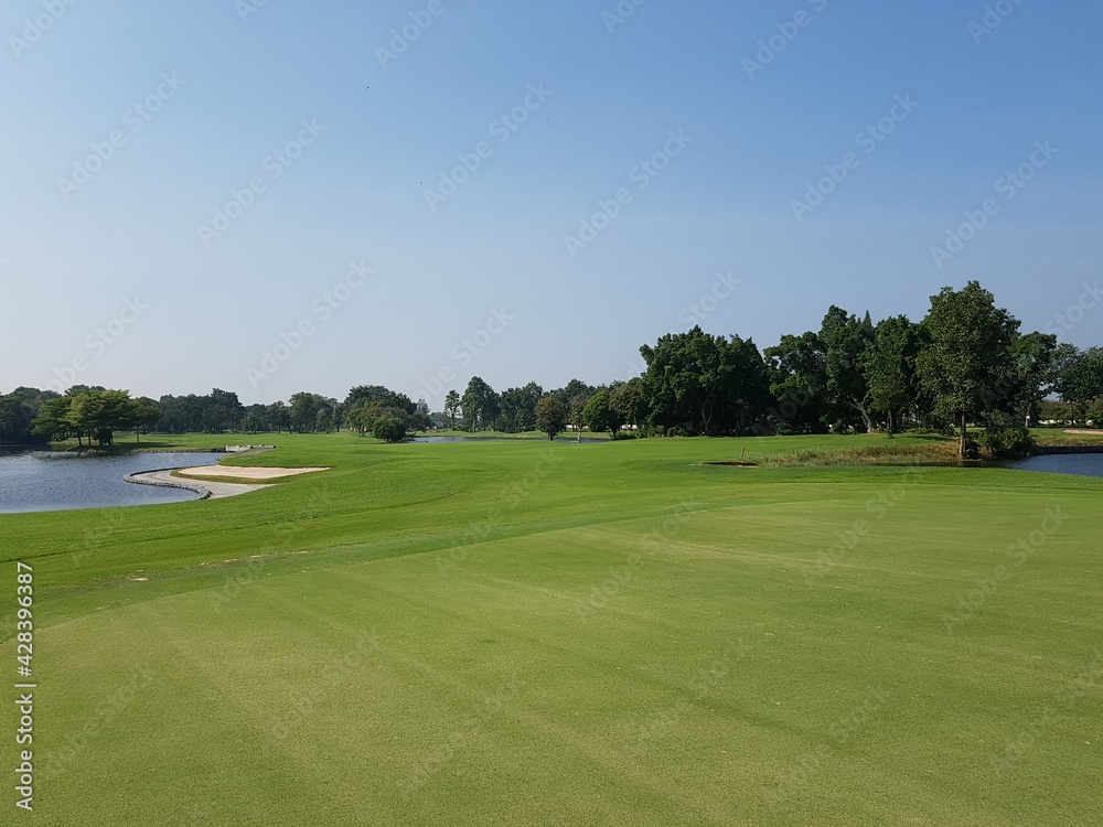 A golf course with a white flag on its hole and a pond and clear sky. A golf course with a white flag on its hole and a pond and clear sky.