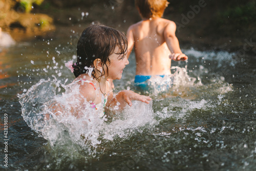Happy summertime  healthy childhood concept. Children playing  splashing  jumping and having fun in a river in summer. Selective focus on one kid. Horizontal shot.