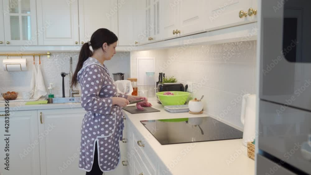 Woman cooking dinner in modern white clean kitchen, cutting meat on cutting board. High quality 4k footage Woman cooking dinner in modern white clean kitchen, cutting meat on cutting board. High quality 4k footage