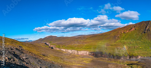 Panoramic view of beautiful colorful Icelandic landscape and biggest canyon in Iceland called Hafrahvammagljufur with waterfall, at sunny summer day with blue sky.