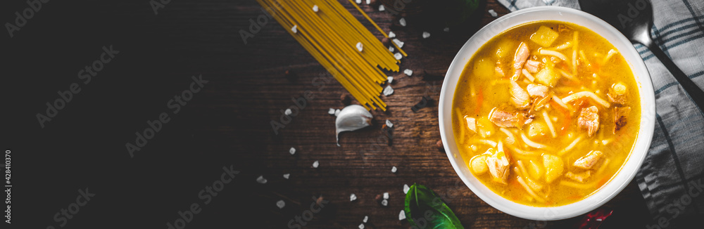 Chicken soup with noodles and vegetables in white bowl on wooden table background Chicken soup with noodles and vegetables in white bowl on wooden table background