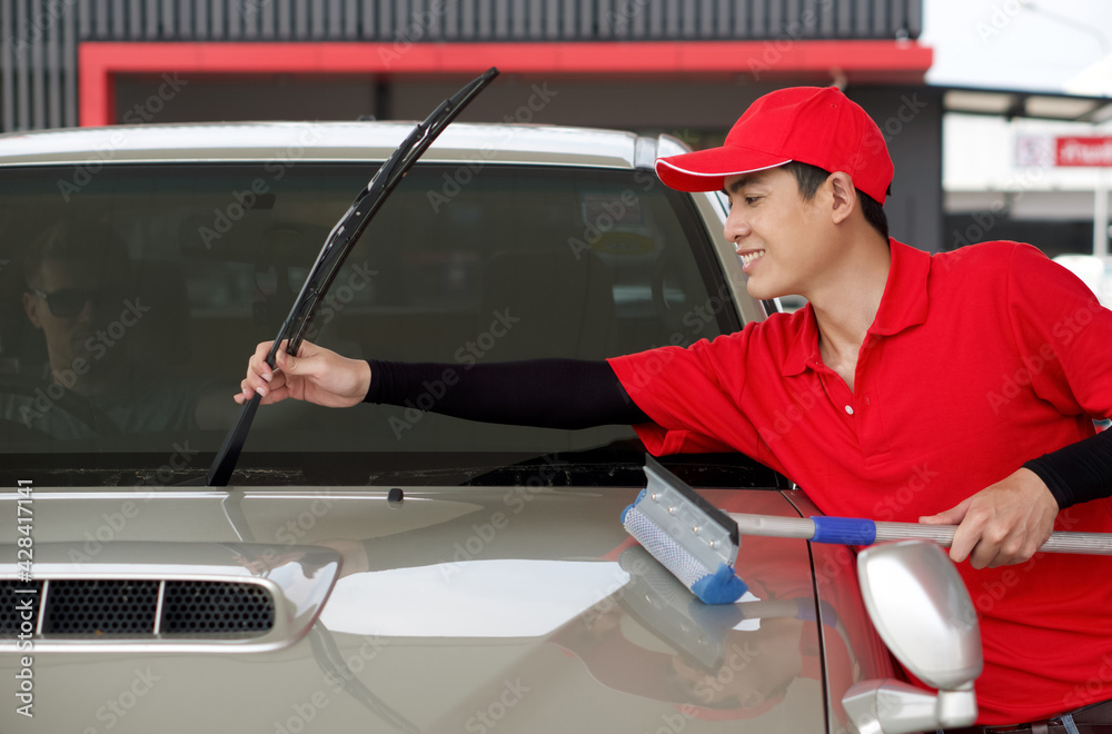 An Asian gas station worker raises the windshield wipers to clean the