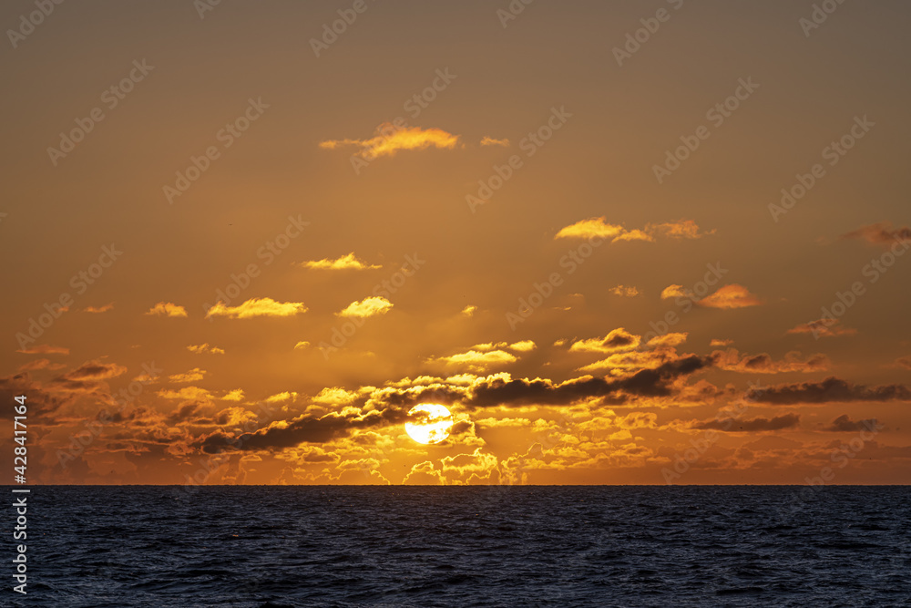 Warm and romantic sunset on the North Sea with small clouds hiding half of the sun