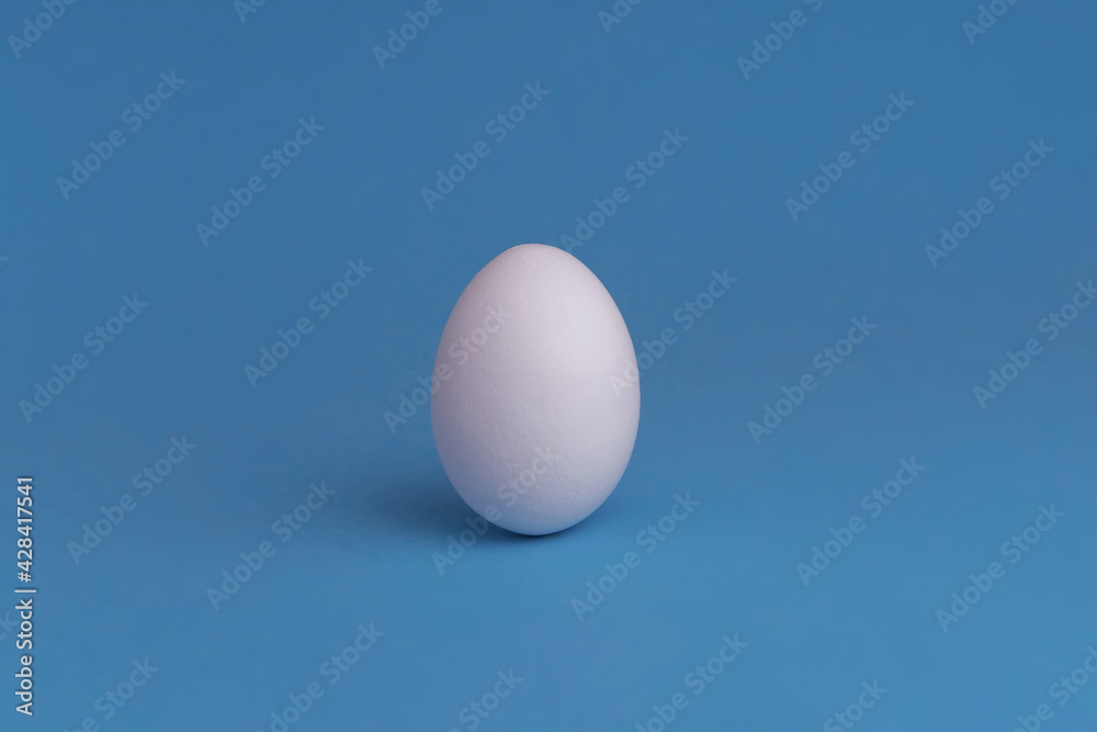 A white egg on a blue background. The concept of minimalism. Side view. A card with a copy of the place for the text. A white egg on a blue background. The concept of minimalism. Side view. A card with a copy of the place for the text.