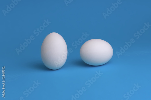 White eggs on a blue background. The concept of minimalism. Side view. A card with a copy of the place for the text.