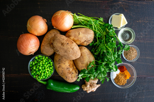 Samosa Potatoes Ingredients on a Dark Wood Background: Raw potatoes, onions, peas, herbs, and spices on a wooden table