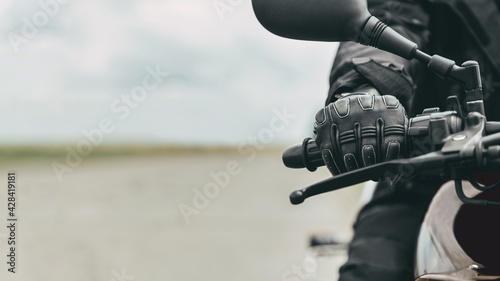 Hand of a man in protective motorcycle gloves holds a black motorcycle, close up