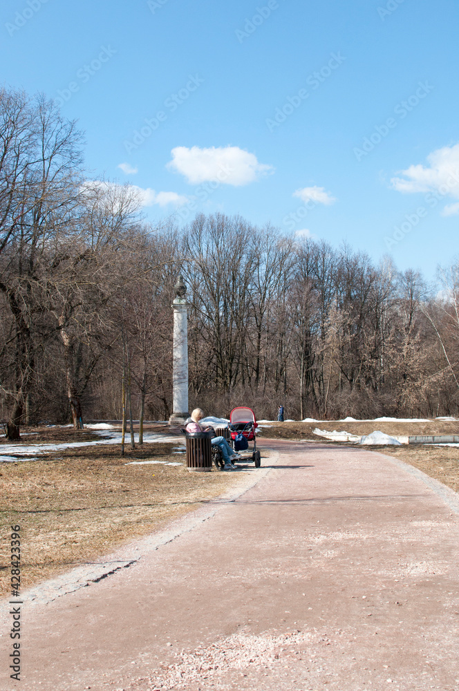 View of the park path, free of snow, bench and people in the park.