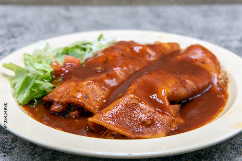 Chicken enchiladas smothered in tasty red sauce on a plate makes for a filling and hearty entree. Chicken enchiladas smothered in tasty red sauce on a plate makes for a filling and hearty entree.