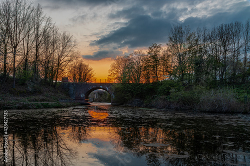 Colorful sunset and reflections in the water in the Frontenpark (English: Fronten Park) in Maastricht. This park is recently re-opened after restorations of the ancient walls and the old train bridge photo