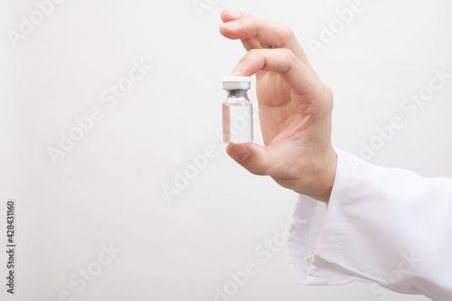 白衣を着た人が持つガラス瓶に入ったワクチン、医薬品