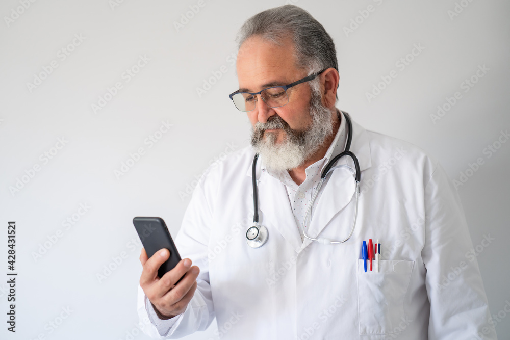 Portrait of senior doctor in white coat looking his smart phone on white background. Portrait of senior doctor in white coat looking his smart phone on white background.