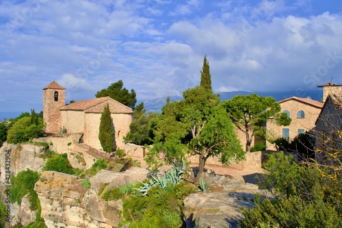 Village with romanesque church of Santa Maria de Siurana on top of rock, view into valley, mountains on the background. Blue sky with white clouds. Siurana, Catalonia, Spain.
