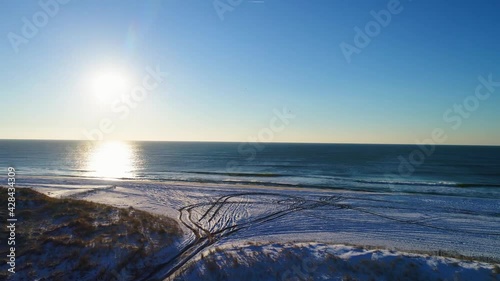 push in shot to shore of beach with snow on the ground and pretty sun over the ocean