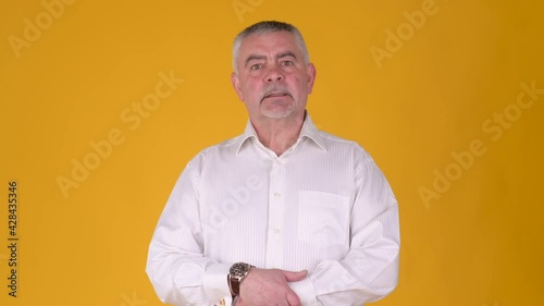 middle aged man in white shirt eagerly awaits checking time on yellow studio background