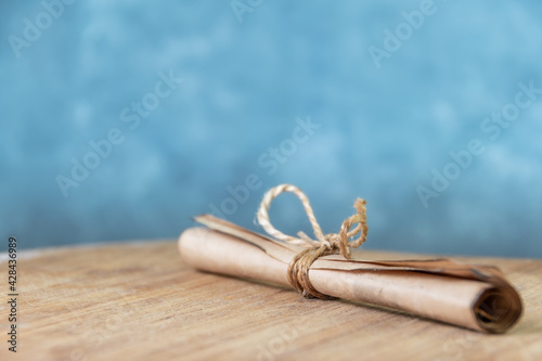 Roll of vintage parchment tied with rope on wooden. Blue wall as background
