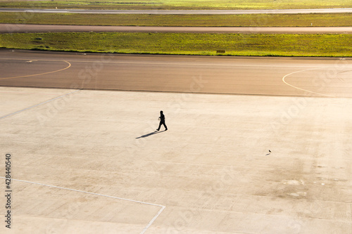 Silhouette of man walking in the distance and small birds on airport runway.