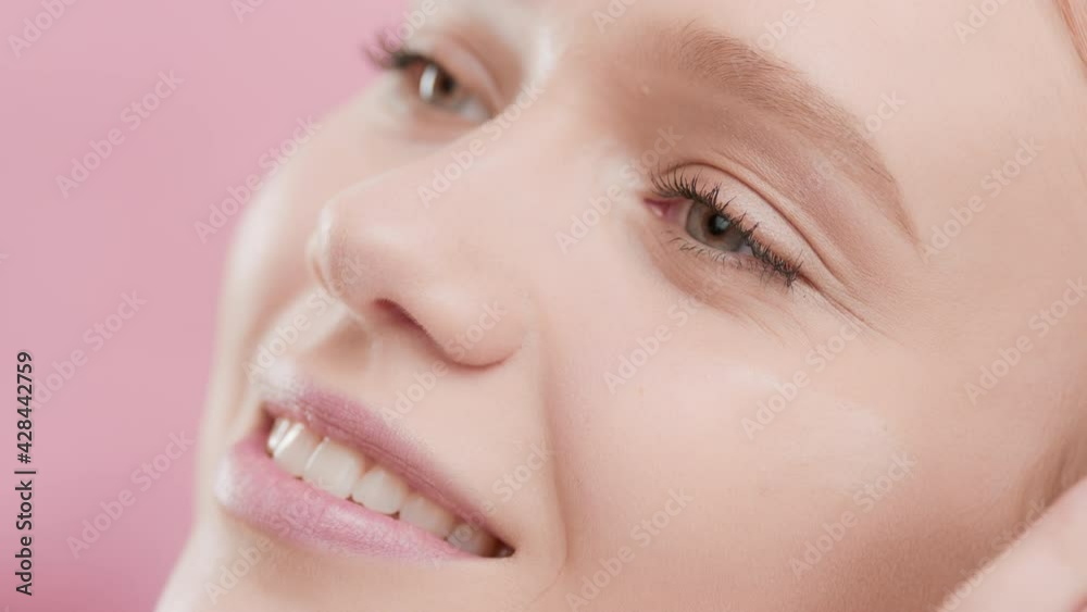 Young beautiful Caucasian skin care woman puts moisturizer on her face smiling wide for the camera against pink ripple background | Moisturizer putting on shot for face care commercial Young beautiful Caucasian skin care woman puts moisturizer on her face smiling wide for the camera against pink ripple background | Moisturizer putting on shot for face care commercial