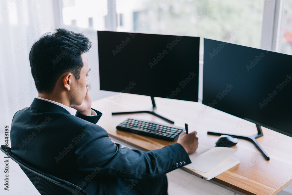 Asian business people are focused on working while on the phone. A computer with two blank screens Asian business people are focused on working while on the phone. A computer with two blank screens