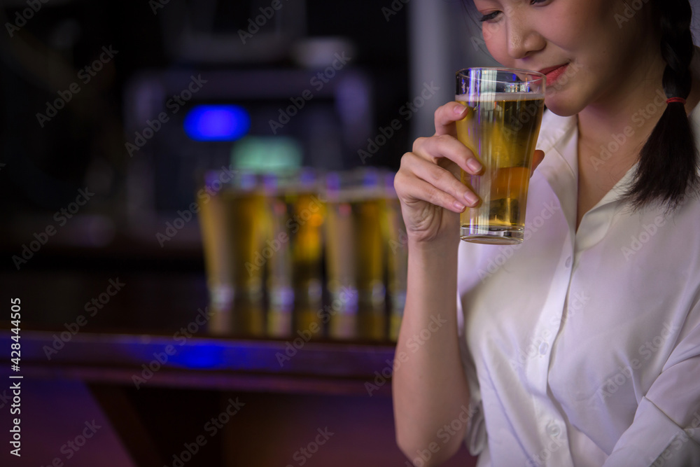 Beautiful Asian woman holding a glass of beer close up on background inside bar.
