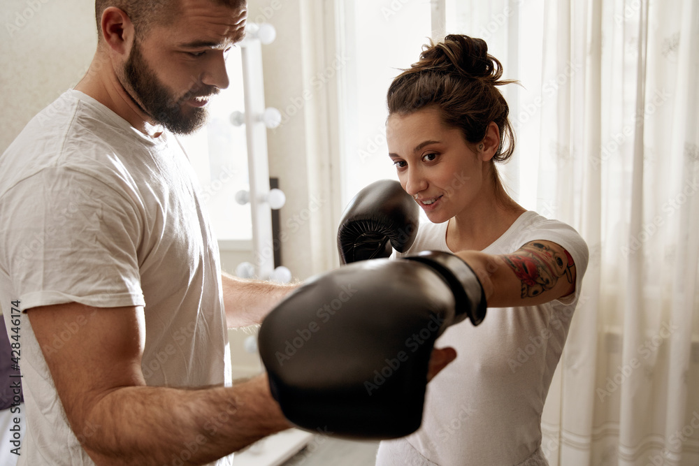 Man helping to his wife wearing gloves to learn how to do boxing techniques Man helping to his wife wearing gloves to learn how to do boxing techniques