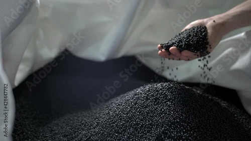 A man pours black polymer granules from his hands in a garbage recycling plant
