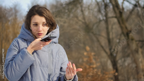 Foto Lady in blue coat is sending audio voice message explaining something on smart phone at outdoor talking to mobile assistant