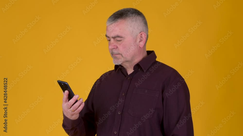 Handsome adult man uses smartphone texting messages in social media on yellow studio background. Elderly people and modern technologies. Handsome adult man uses smartphone texting messages in social media on yellow studio background. Elderly people and modern technologies.