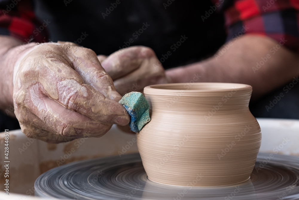 Male hands cleaning with sponge pottery on a potter wheel. Male hands cleaning with sponge pottery on a potter wheel.