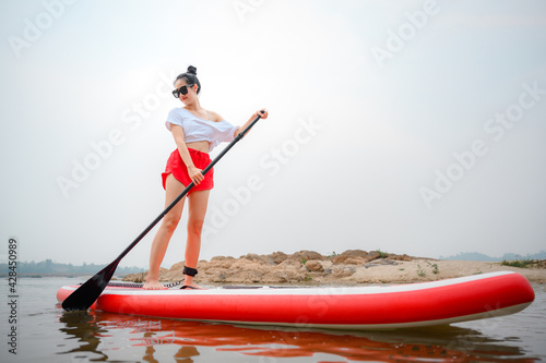 Beautiful Asian girl on a paddleboard Stand paddle in the ocean on the beach. Asian young women enjoying water sports