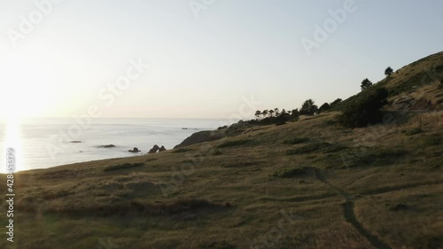 Worn trail on grassy hillside along coastal cliffs at sunset