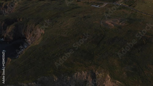 Worn trails on grassy hillside along coast at sunset