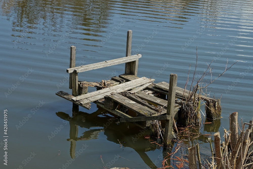 Fototapeta premium old broken gray wooden footbridge over lake water near the shore