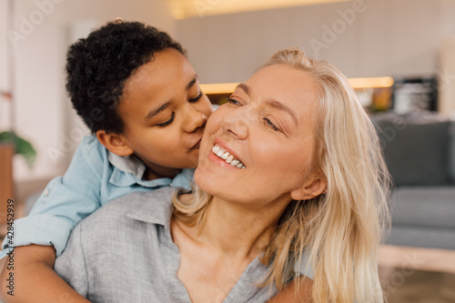 Boy embracing his senior mother at the shoulders and kissing her at the chic