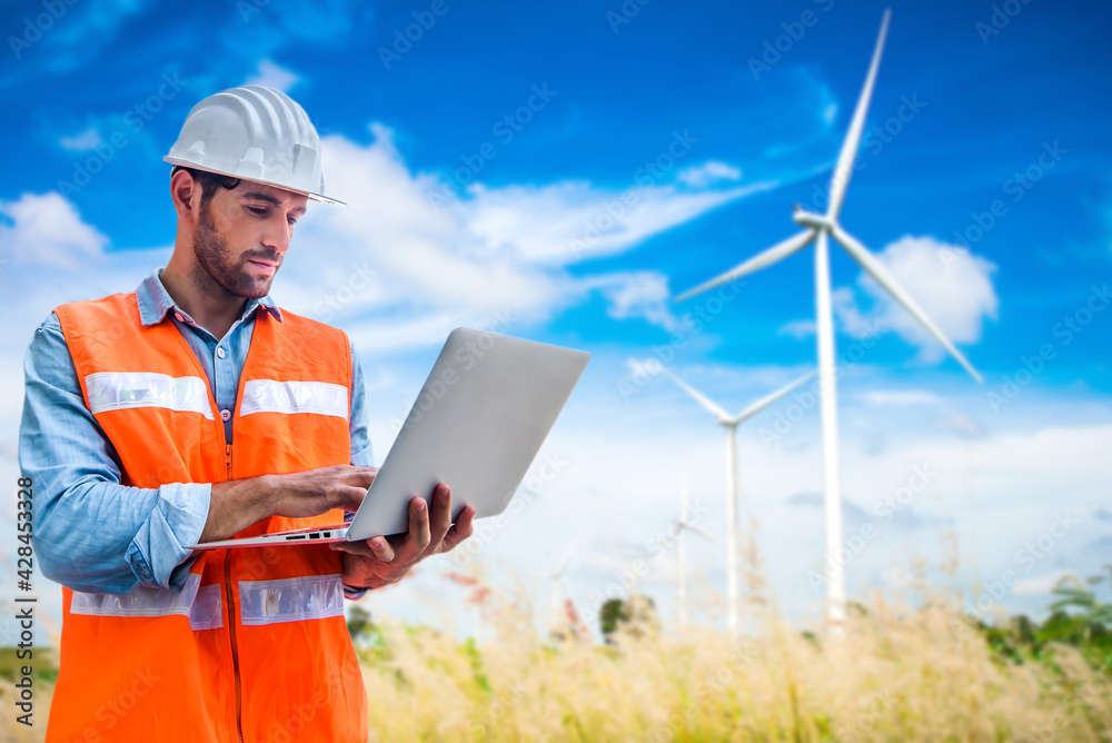 Engineering man using laptop to checking wind turbine generator of electricity at outdoor, blue sky and cloudy background