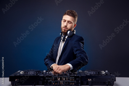 Man DJ in dark suit play music on a Dj's mixer. Studio shot. Dark blue background
