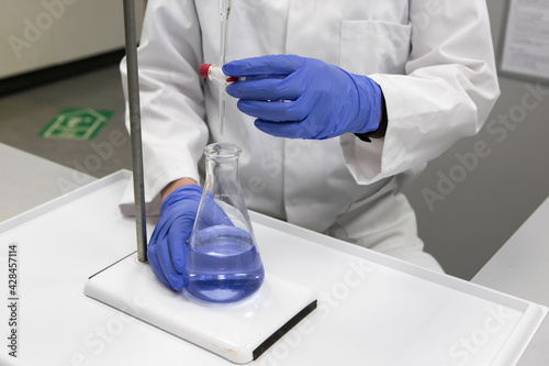 Chemist with gloved hands and a white labcoat in a laboratory analysing a sample by titration  photo