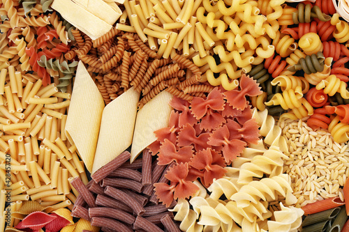 Selection of dried Italian pasta types with tricolour and whole wheat shapes. Healthy carbohydrate food concept. Abstract background, flat lay, top view.
