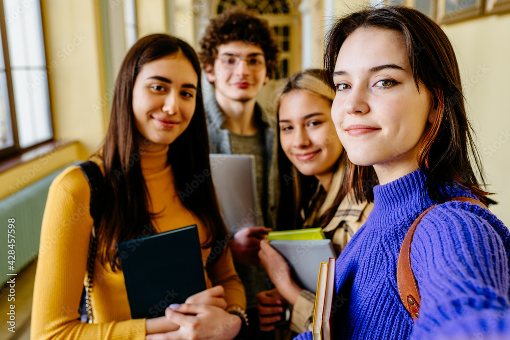 Beautiful young brunette woman making selfie with friends and smiling. Indoor portrait of joyful smiling students having fun after lessons and taking photo in university campus. Beautiful young brunette woman making selfie with friends and smiling. Indoor portrait of joyful smiling students having fun after lessons and taking photo in university campus.