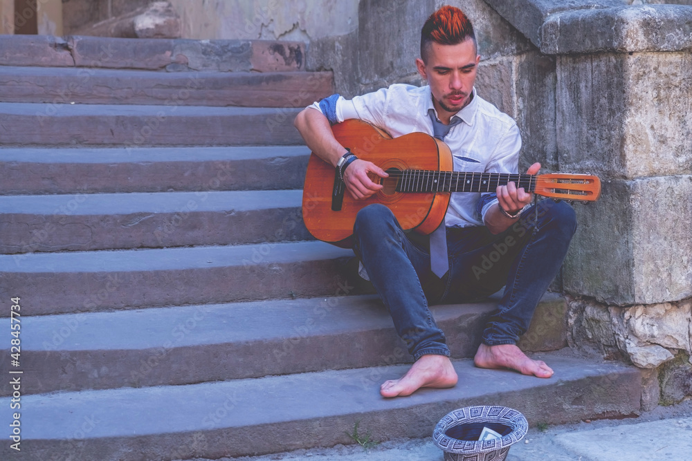 Young man playing the guitar outdoors in old European city. Copy space for design or text. Horizontal image.