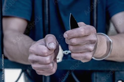 Handcuffed man with a knife imprisoned for crime, punished for serious villainy. Arrest, gangster, pain concept. Close up. Selective focus.