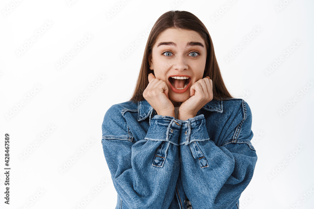 Surprised and excited girl screams from great awesome news, looking amazed and happy, rejoicing, shouting from joy and happiness, standing over white background Surprised and excited girl screams from great awesome news, looking amazed and happy, rejoicing, shouting from joy and happiness, standing over white background