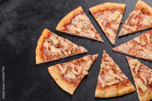 Tasty fresh oven pizza with tomatoes, cheese and pineapple on a dark concrete background