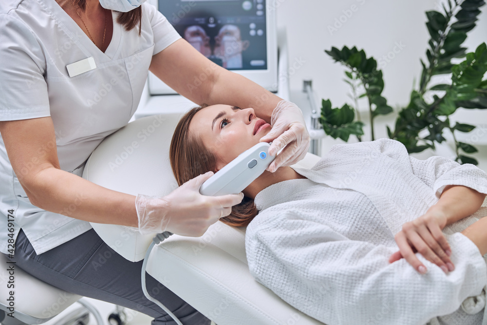Young charming woman in white bathrobe receiving face skin care in spa center Young charming woman in white bathrobe receiving face skin care in spa center