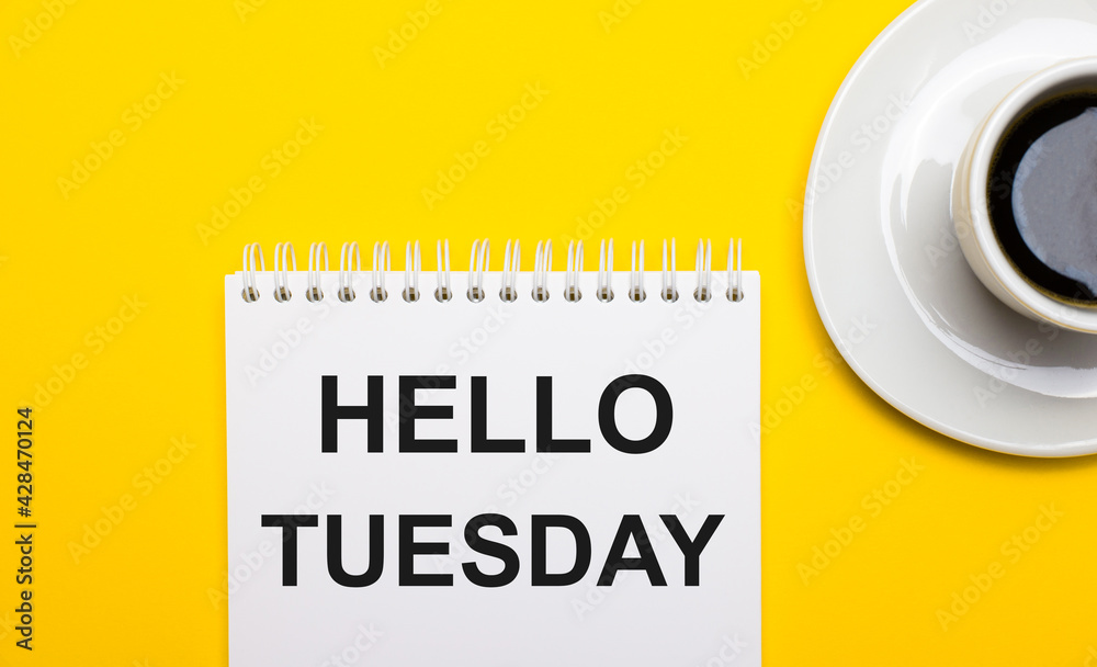 On a bright yellow background, a white cup with coffee and a white notepad with the words HELLO TUESDAY