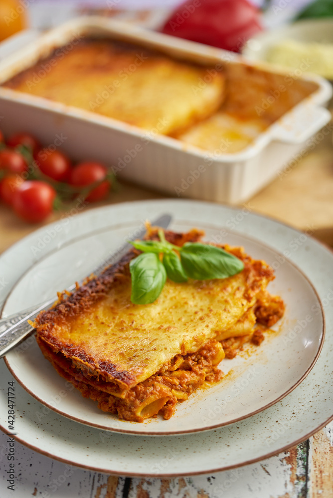 Homemade tasty meat lasagna with fresh basil and parmesan cheese in a plate on wooden background Homemade tasty meat lasagna with fresh basil and parmesan cheese in a plate on wooden background