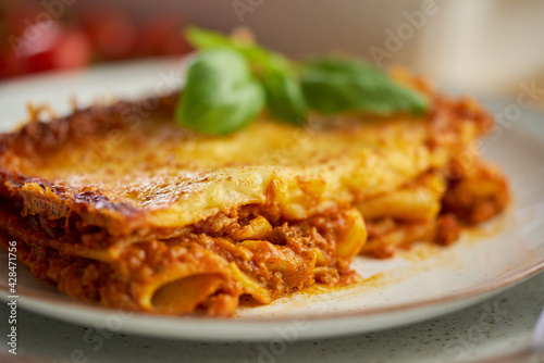 Homemade tasty meat lasagna with fresh basil and parmesan cheese in a plate on wooden background