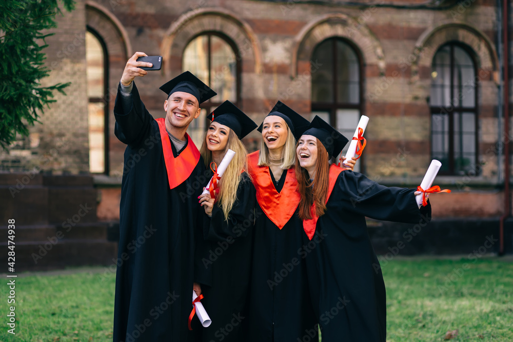 Obraz premium group happy graduates students use mobile phone to take selfie together. After receiving diplomas.