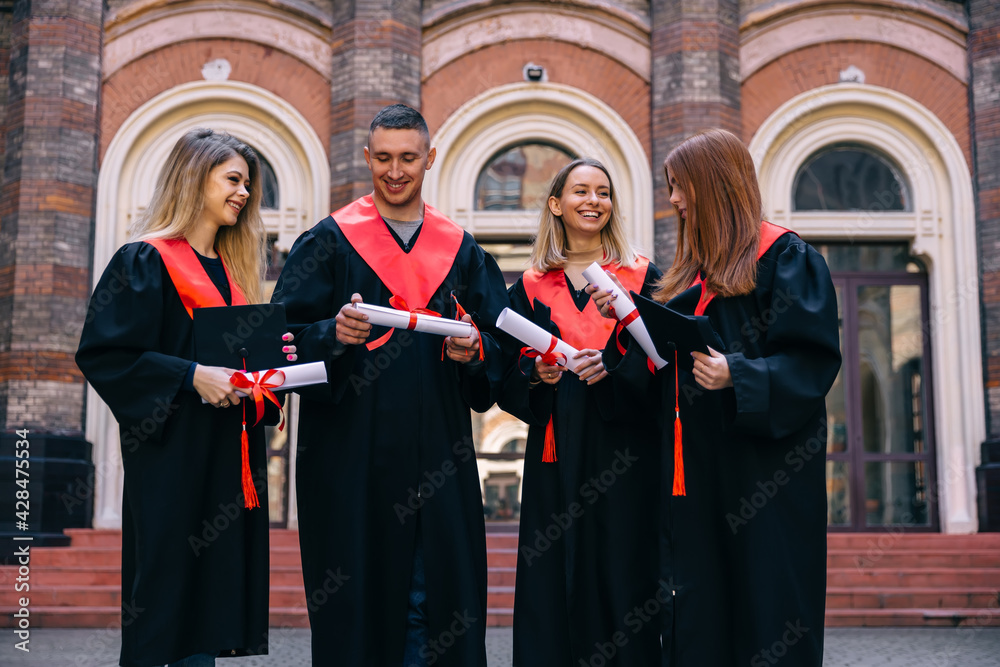 Successful graduation from university, education concept. A group of happy university graduates in black coats, standing with diplomas in their hands, smiling.